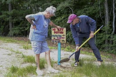 Intern and Volunteer Coordinator, Billie-Joe Gibbons, left, holds a turtle sign as Jay Whitestone, a volunteer, pounds the sign into the sand near turtle nests behind Wareham High School.