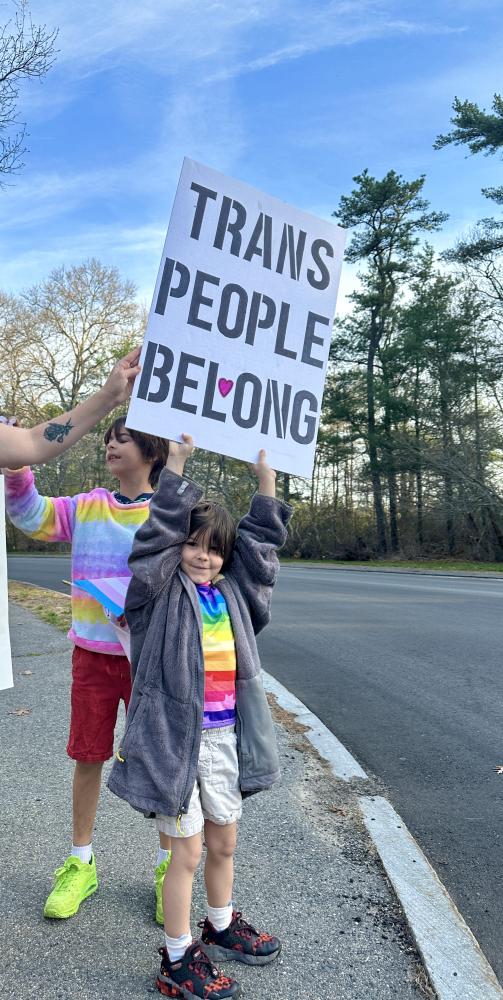 A child stands outside of Nichols Middle School with a sign saying “trans people belong.”