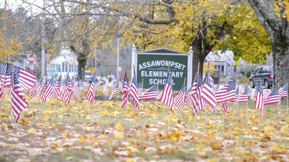 American flags flutter in the wind in front of the Assawompset Elementary School. Photo by Sam Tucker