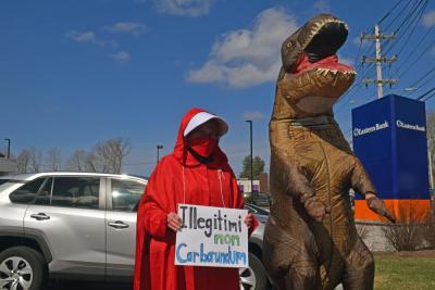 A woman wearing the Handmaid's Tale costume next to a T-rex.