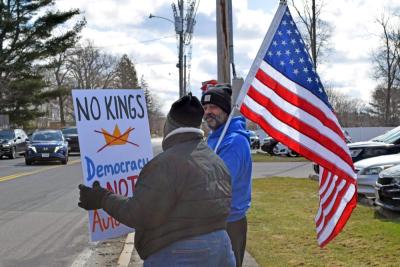 One protester holds a sign with another holding the American flag in the background.
