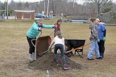 The girl scouts gather dirt to plant by the edge of the fence.