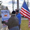 One protester holds a sign with another holding the American flag in the background.