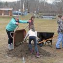 The girl scouts gather dirt to plant by the edge of the fence.