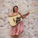 sara achorn stands against a wall with her guitar 