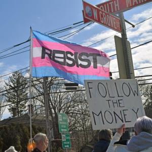 A protester waves the trans flag demanding resistance.