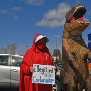 A woman wearing the Handmaid's Tale costume next to a T-rex.
