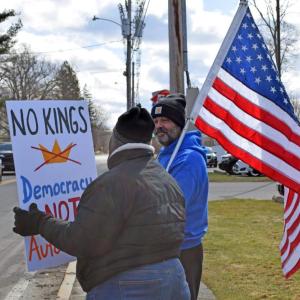 One protester holds a sign with another holding the American flag in the background.