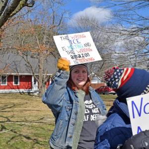 A woman holds a sign commenting on current politics and global change.