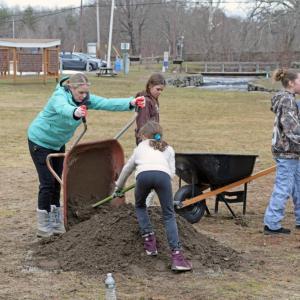 The girl scouts gather dirt to plant by the edge of the fence.